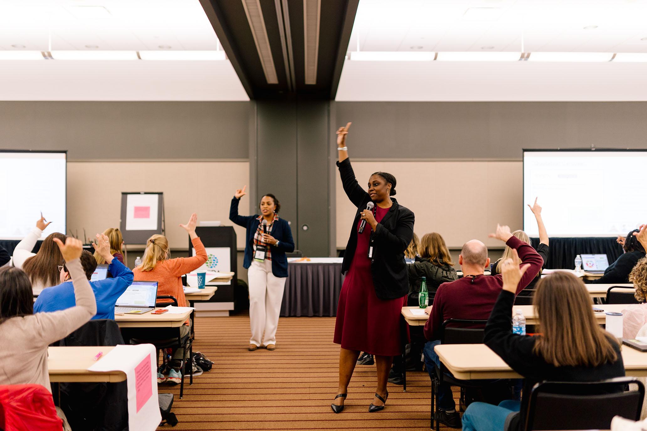 Two conference presenters stand in a conference session with their arms raised