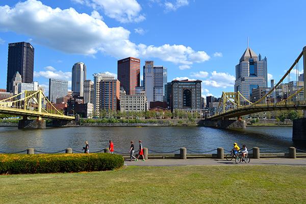 Two bridges going across a river with a city skyline in the background.