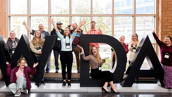 group of conference attendees posing around a large sculpture of the word WIDA