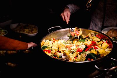 someone dishing up pasta salad from a buffet