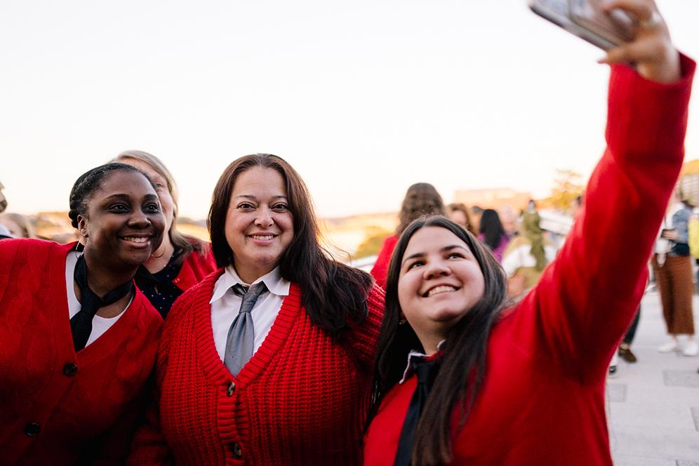 Three people together wearing red cardigans smile for a selfie