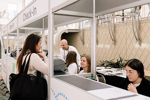 a crowd of people waiting and talking at conference check-in booths