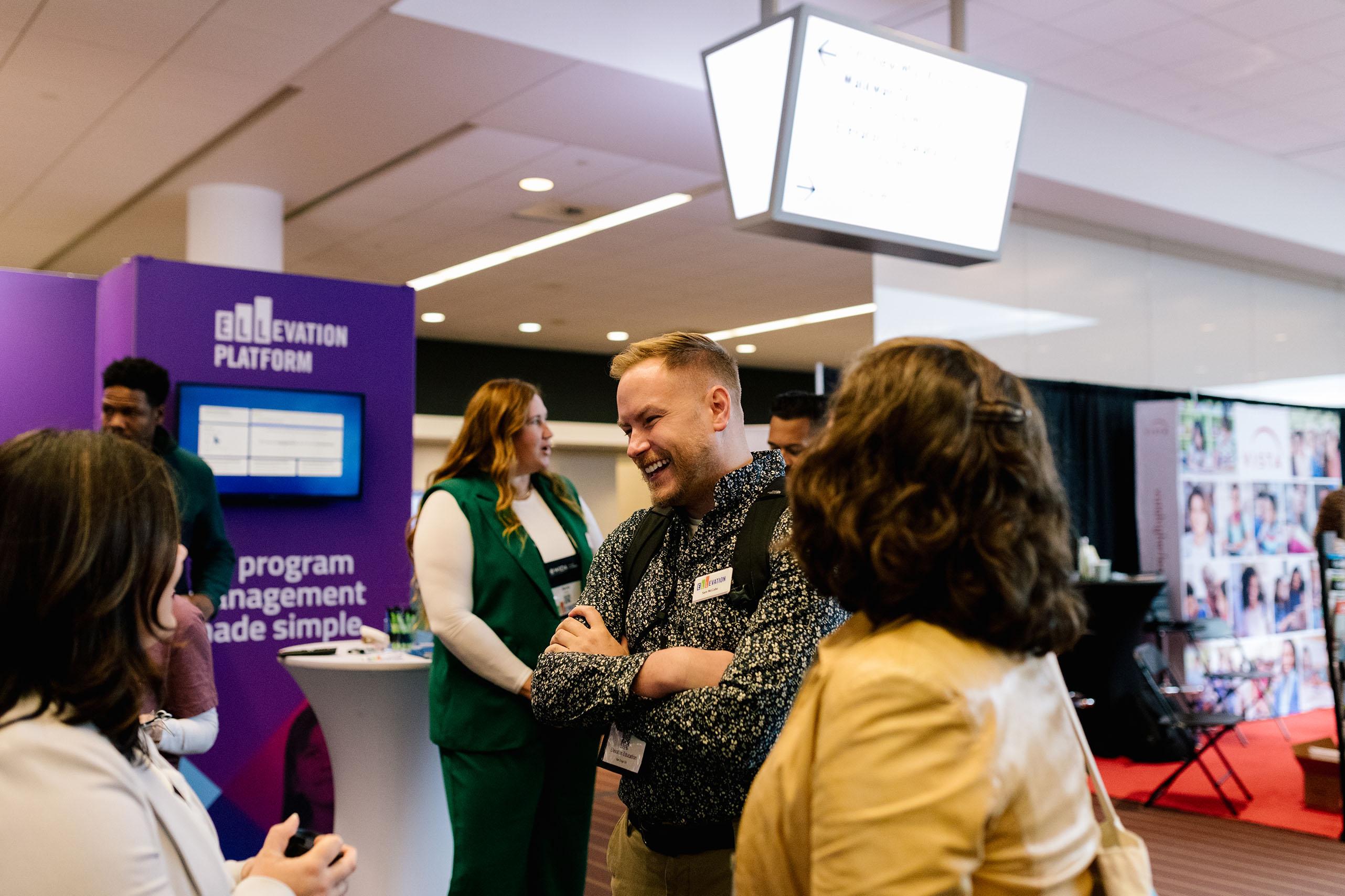 People talking and smiling at a conference sponsor booth.